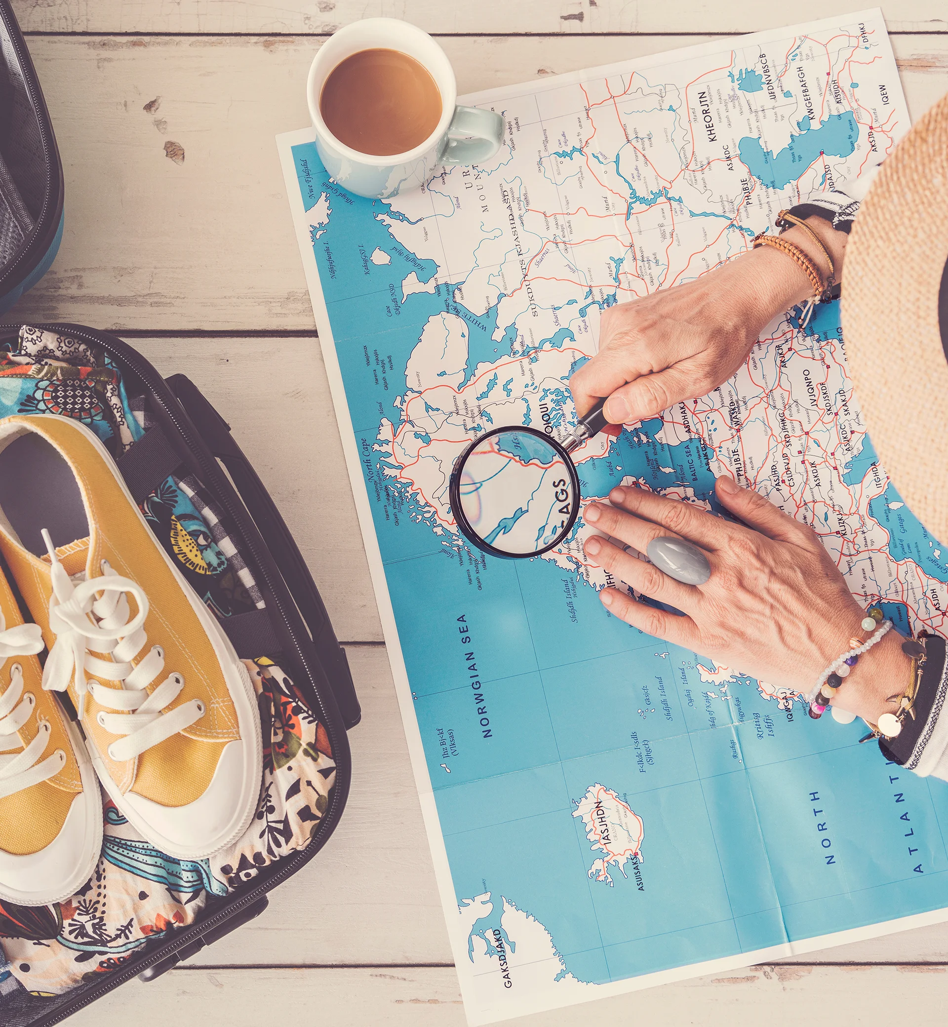 Imagen de una persona mirando un mapa con lupa y con las maletas de viaje a medio terminar.